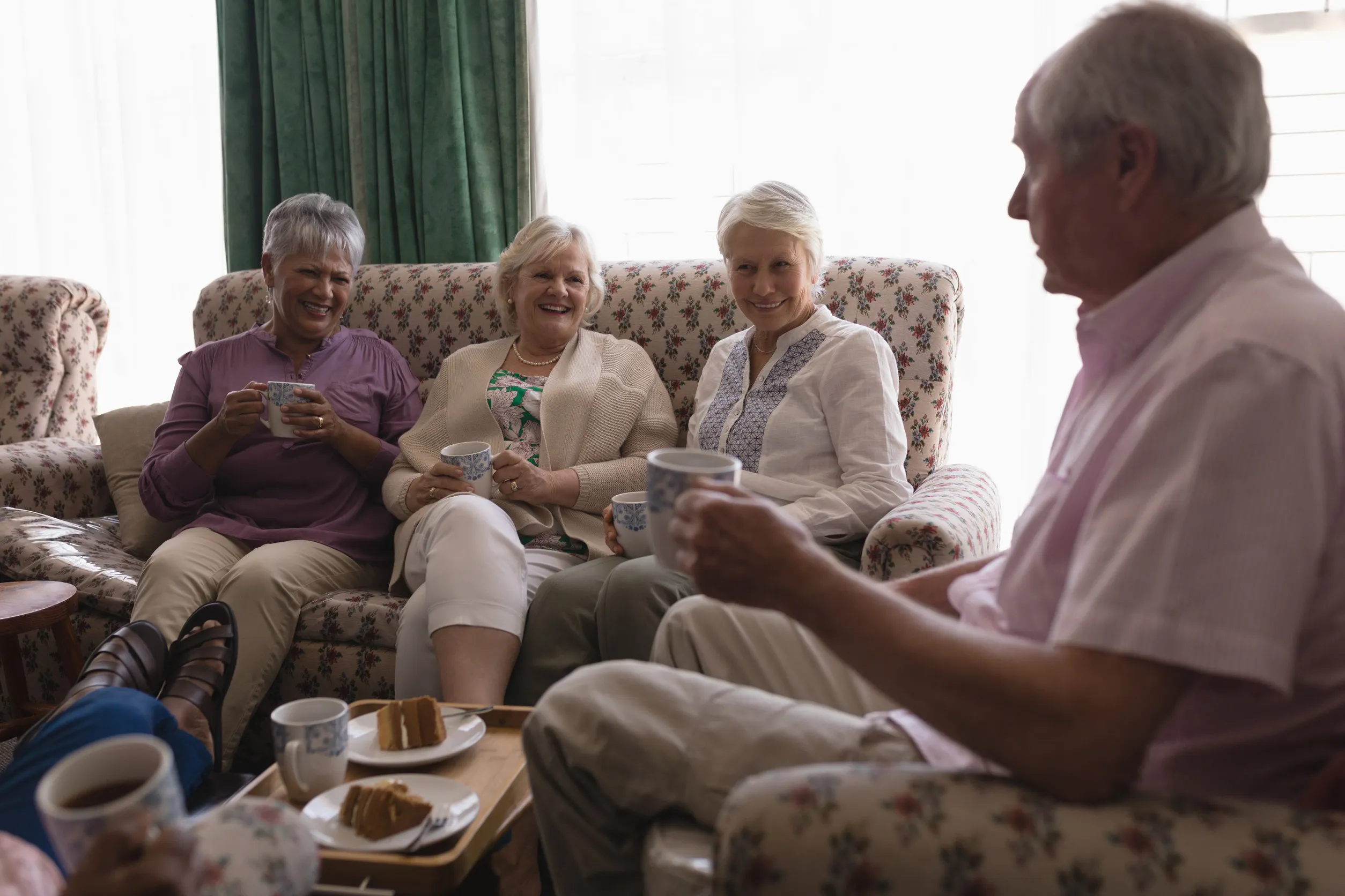 Side view of senior people having coffee and cake in living room at home